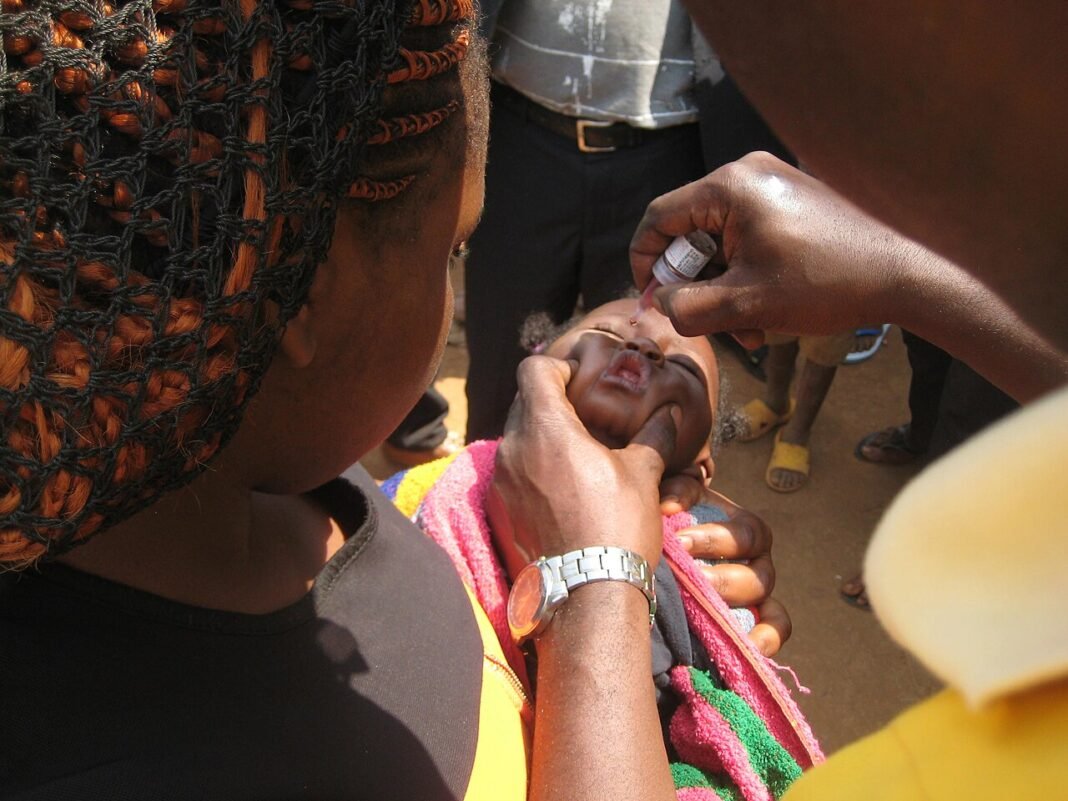 Health worker giving oral polio vaccine drops to a baby held by her mother