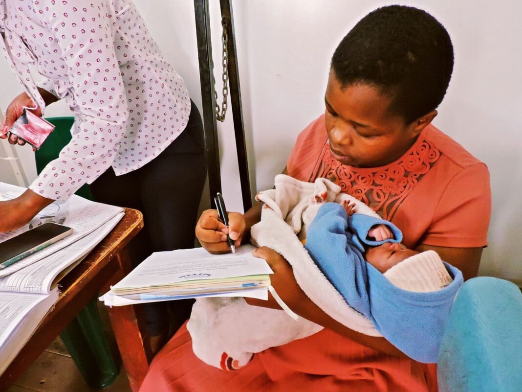 Mother holding her newborn baby while filling in a health record at a clinic