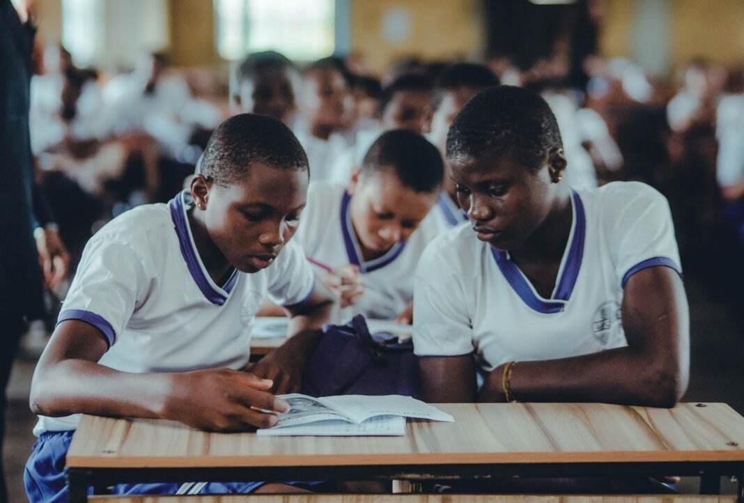 African secondary school students in uniform revising together from a textbook in a classroom
