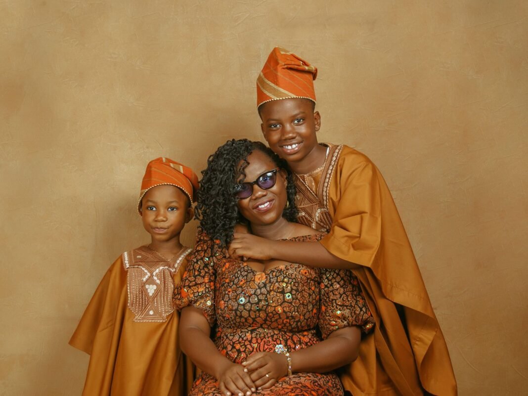Smiling Yoruba mother with her two sons dressed in traditional agbada and fila caps