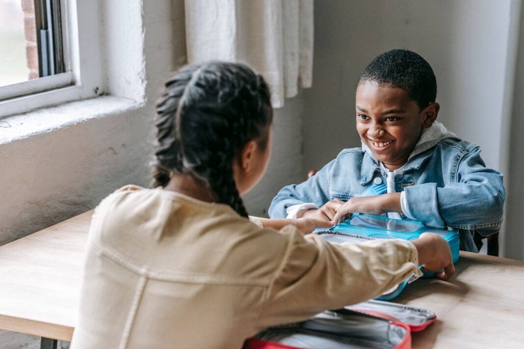 Smiling schoolboy opening his lunch box at a classroom table during break time