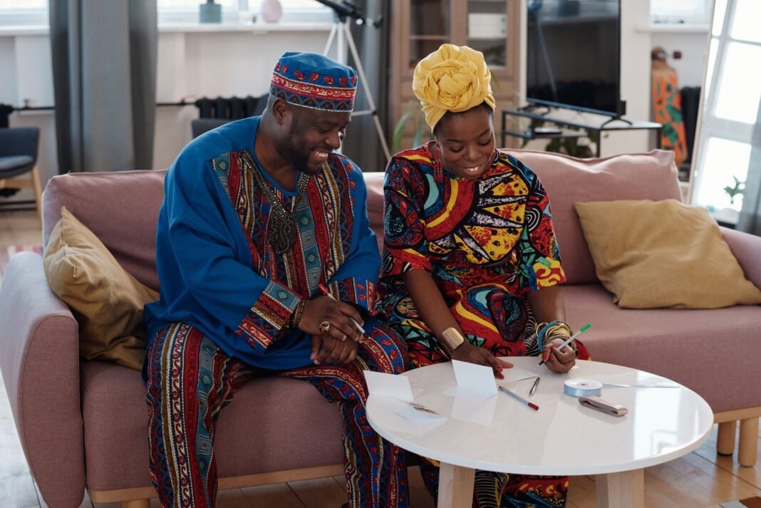 Smiling African couple in traditional attire sitting together on a sofa at home